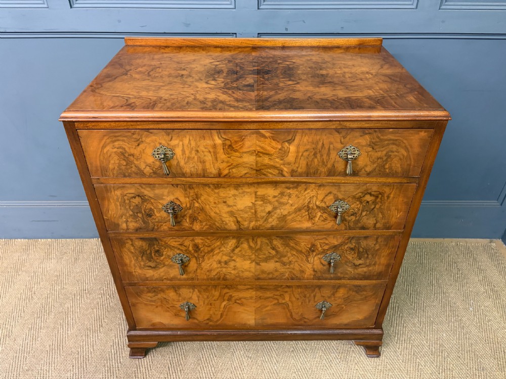 An Art Deco burr walnut chest of four full-width drawers featuring figured veneer panels, decorative brass drop handles, and low bracket feet. View III
