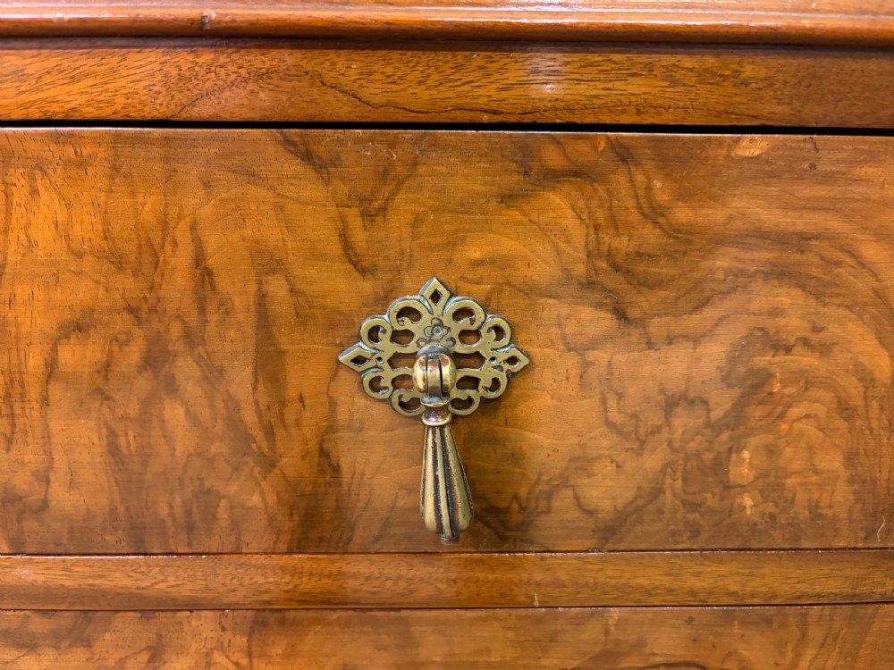 An Art Deco burr walnut chest of four full-width drawers featuring figured veneer panels, decorative brass drop handles, and low bracket feet. View VI