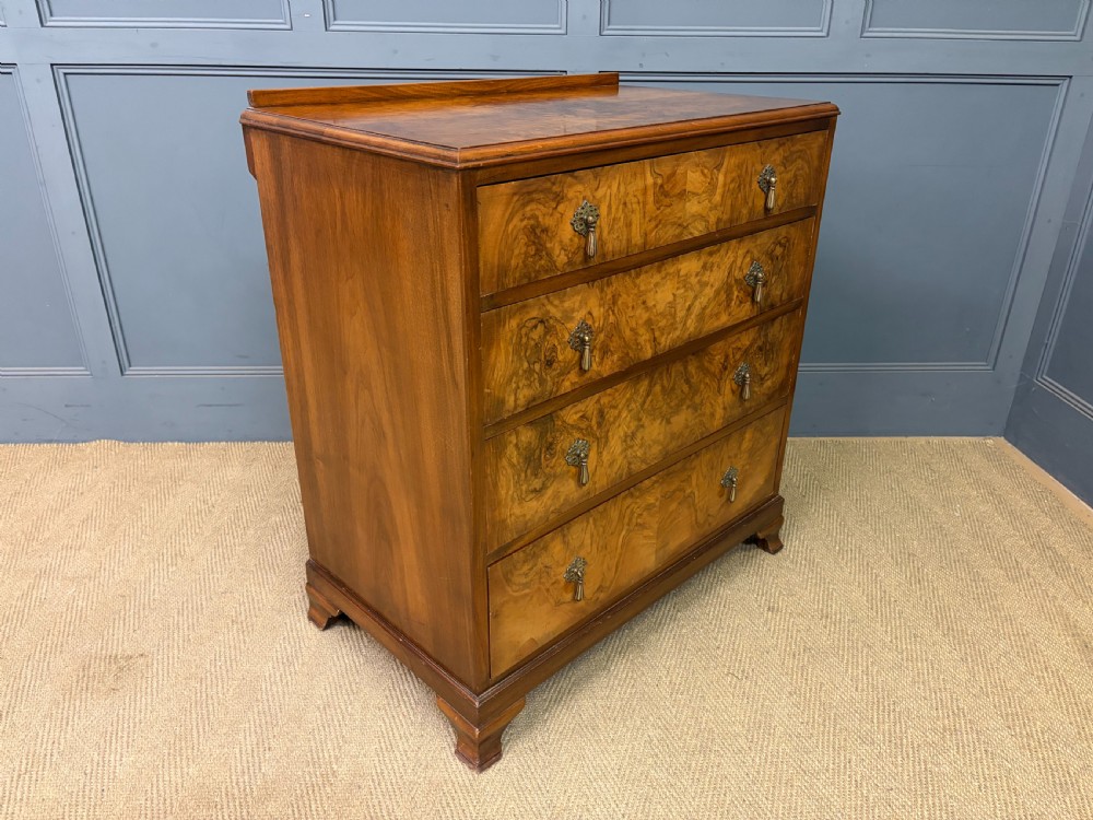 An Art Deco burr walnut chest of four full-width drawers featuring figured veneer panels, decorative brass drop handles, and low bracket feet. View IX