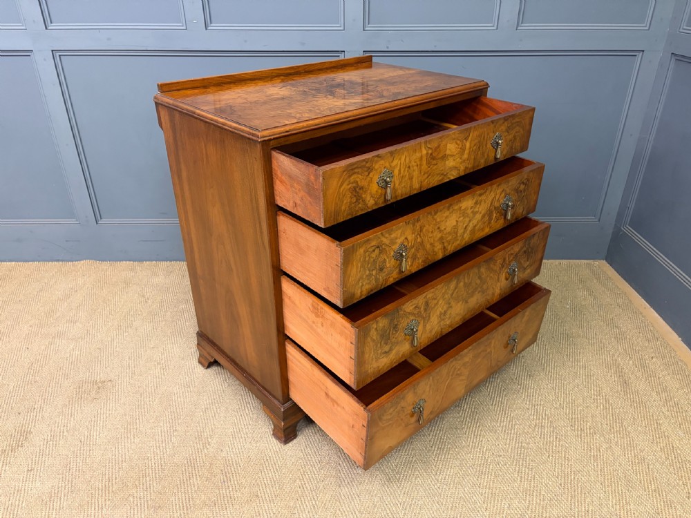 An Art Deco burr walnut chest of four full-width drawers featuring figured veneer panels, decorative brass drop handles, and low bracket feet. View XII