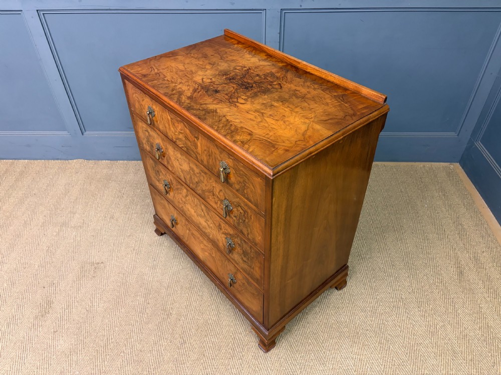 An Art Deco burr walnut chest of four full-width drawers featuring figured veneer panels, decorative brass drop handles, and low bracket feet. View XIII