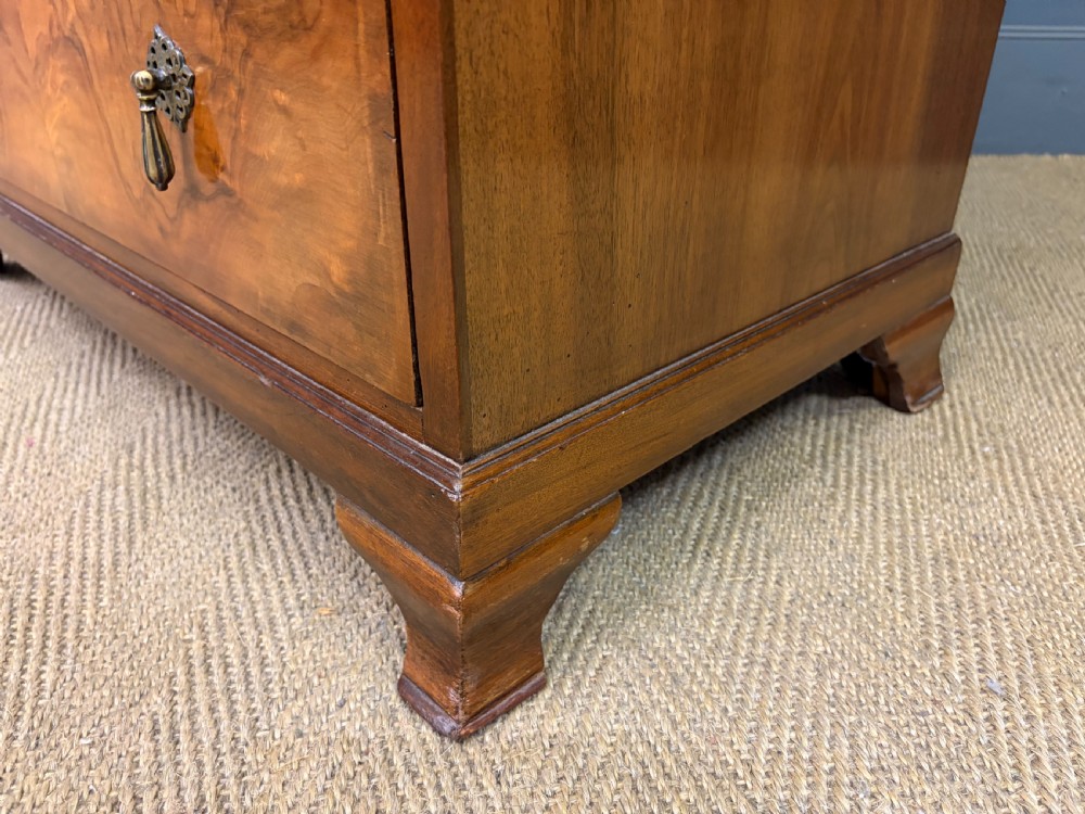 An Art Deco burr walnut chest of four full-width drawers featuring figured veneer panels, decorative brass drop handles, and low bracket feet. View XIV