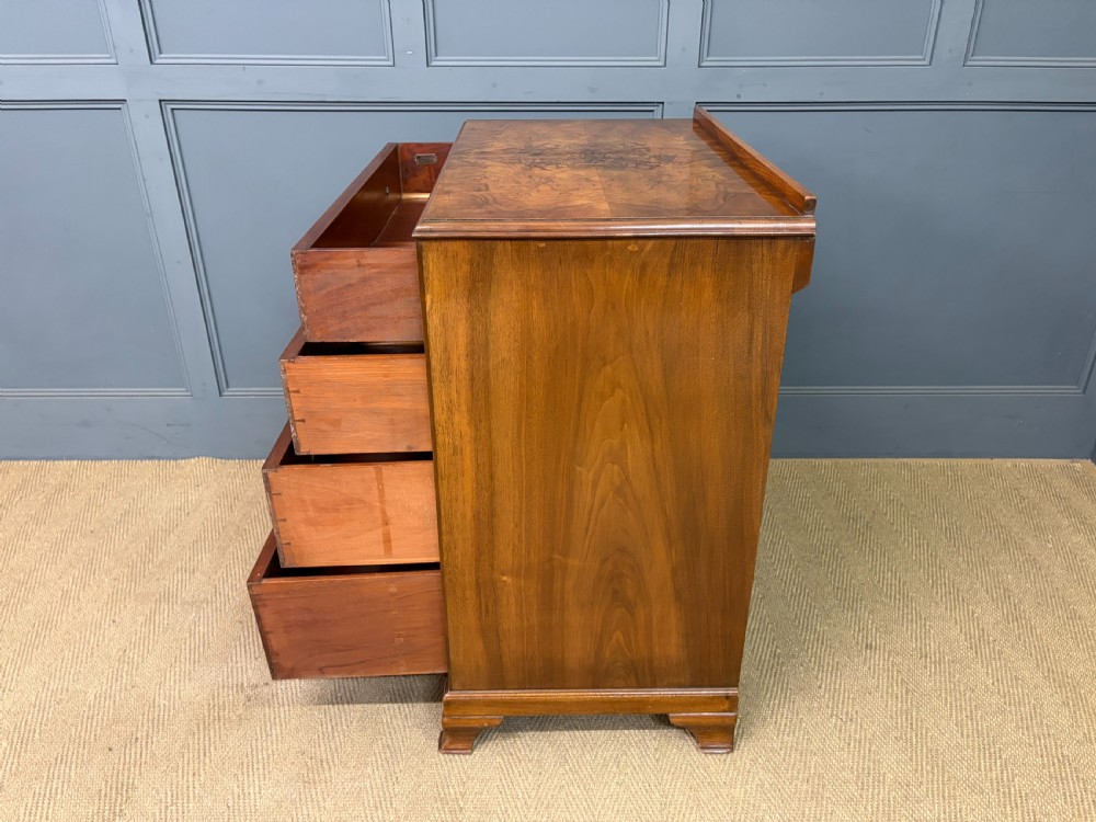 An Art Deco burr walnut chest of four full-width drawers featuring figured veneer panels, decorative brass drop handles, and low bracket feet. View XV
