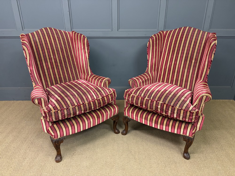 A pair of high-backed wing armchairs upholstered in red and gold striped velvet fabric with carved timber cabriole legs.