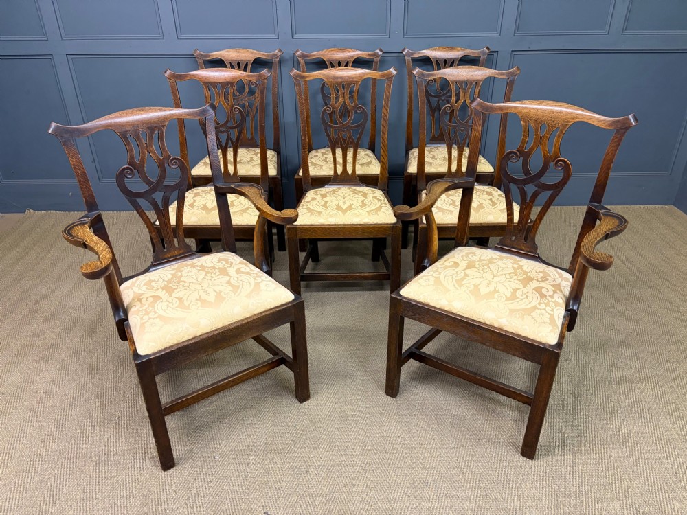 A set of eight brown oak Chippendale dining chairs including two armchairs and six side chairs with patterned fabric drop-in seats.