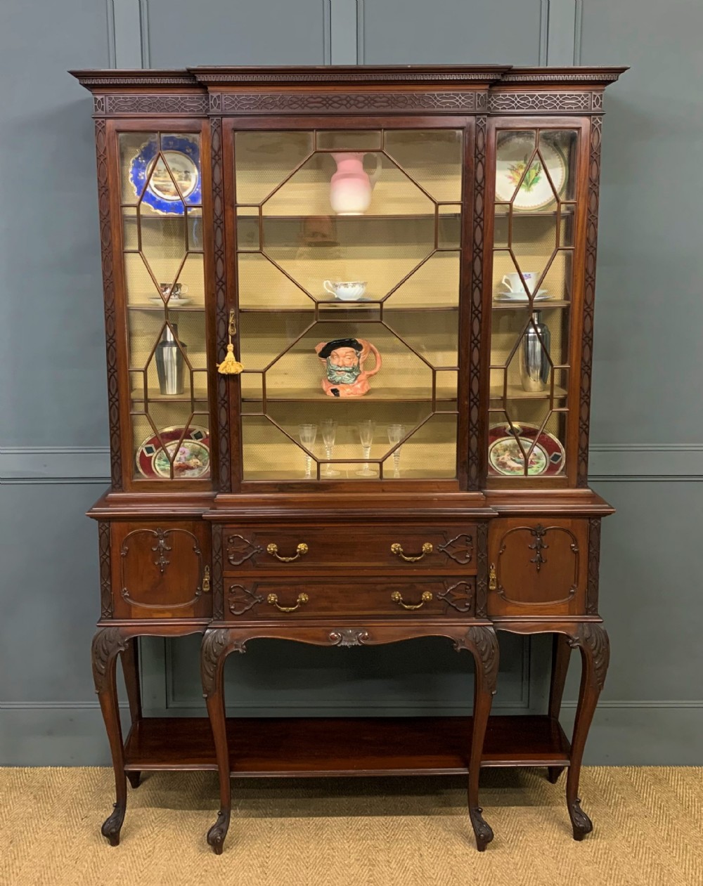 A carved dark mahogany display cabinet featuring astragal glazed doors, lower drawers, carved cabriole legs, and an undertier shelf.