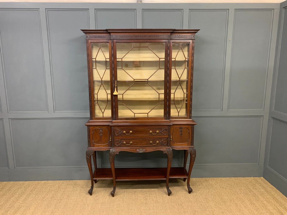 A carved dark mahogany display cabinet featuring astragal glazed doors, lower drawers, carved cabriole legs, and an undertier shelf. View IV