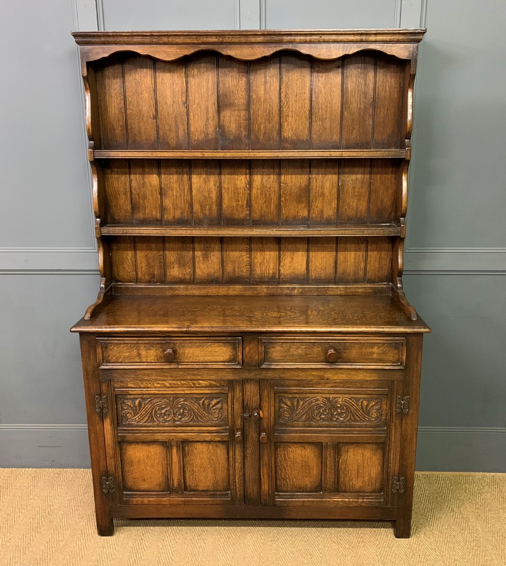 A dark oak Welsh dresser featuring an upper open plate rack with three shelves above a lower cabinet with two drawers and two carved panel doors. View IV