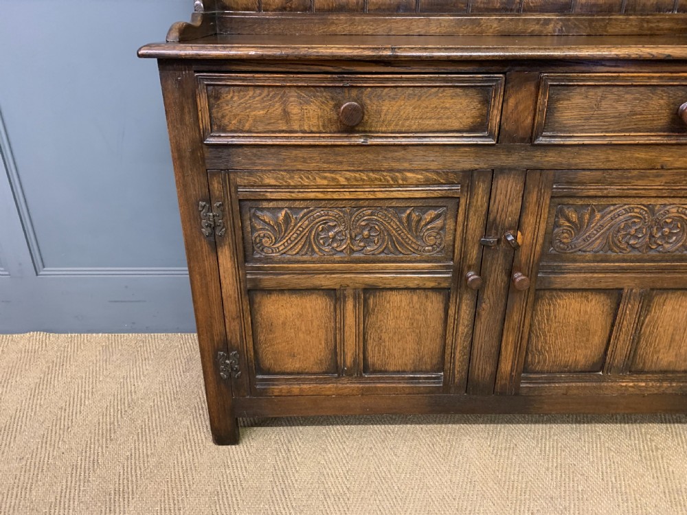 A dark oak Welsh dresser featuring an upper open plate rack with three shelves above a lower cabinet with two drawers and two carved panel doors. View VI