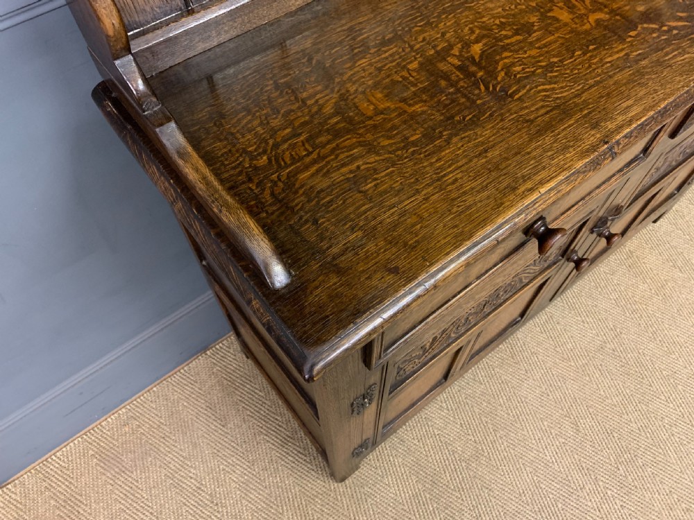 A dark oak Welsh dresser featuring an upper open plate rack with three shelves above a lower cabinet with two drawers and two carved panel doors. View VII