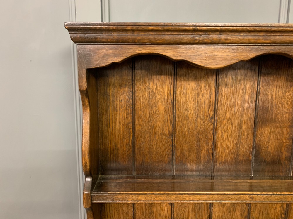 A dark oak Welsh dresser featuring an upper open plate rack with three shelves above a lower cabinet with two drawers and two carved panel doors. View VIII