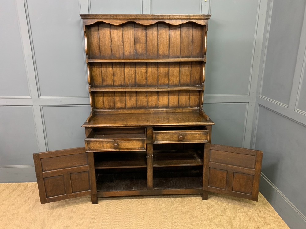 A dark oak Welsh dresser featuring an upper open plate rack with three shelves above a lower cabinet with two drawers and two carved panel doors. View IX