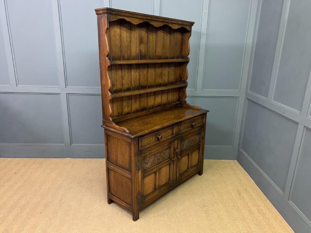 A dark oak Welsh dresser featuring an upper open plate rack with three shelves above a lower cabinet with two drawers and two carved panel doors. View XI