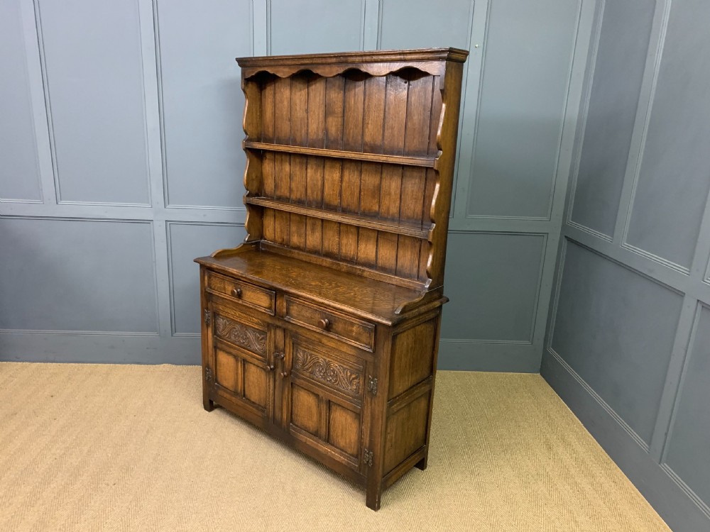 A dark oak Welsh dresser featuring an upper open plate rack with three shelves above a lower cabinet with two drawers and two carved panel doors. View XIII