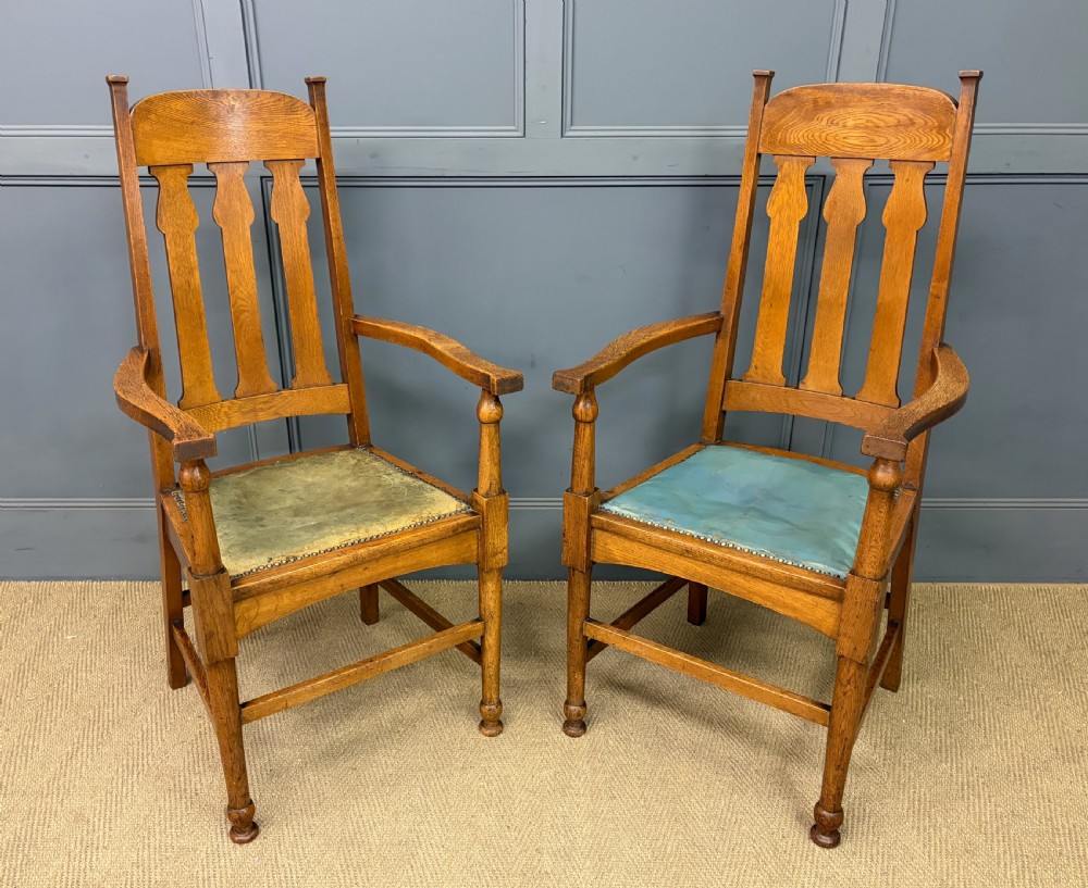 A pair of high-backed Arts and Crafts oak armchairs with vertical back splats and studded leather seats.