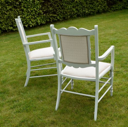 fig 4. A pair of painted pale green Edwardian open armchairs featuring cream upholstered seats, padded backrest panels, turned front legs, and scalloped top rails.