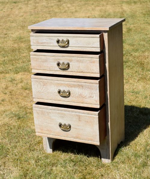 fig 3. A tall Edwardian limed oak chest of drawers with four graduated drawers, brass handles, and a shaped apron base.