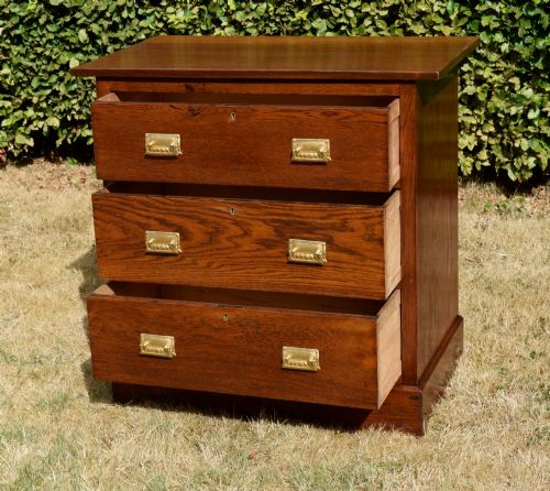 fig 4. A medium-toned oak chest of drawers featuring three drawers with rectangular brass handles resting on a plinth base.