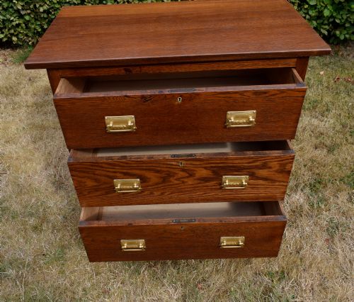fig 5. A medium-toned oak chest of drawers featuring three drawers with rectangular brass handles resting on a plinth base.