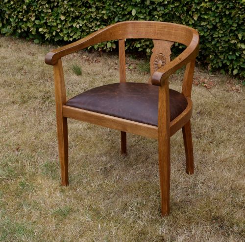 fig 2. An early 20th-century oak desk chair featuring a curved horseshoe backrest, a carved central splat, and a dark brown upholstered seat pad.