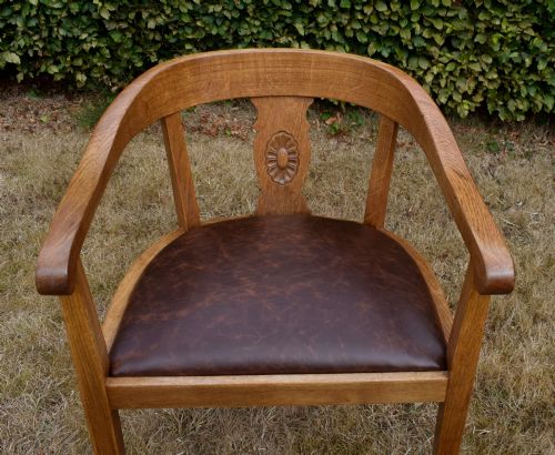 fig 5. An early 20th-century oak desk chair featuring a curved horseshoe backrest, a carved central splat, and a dark brown upholstered seat pad.