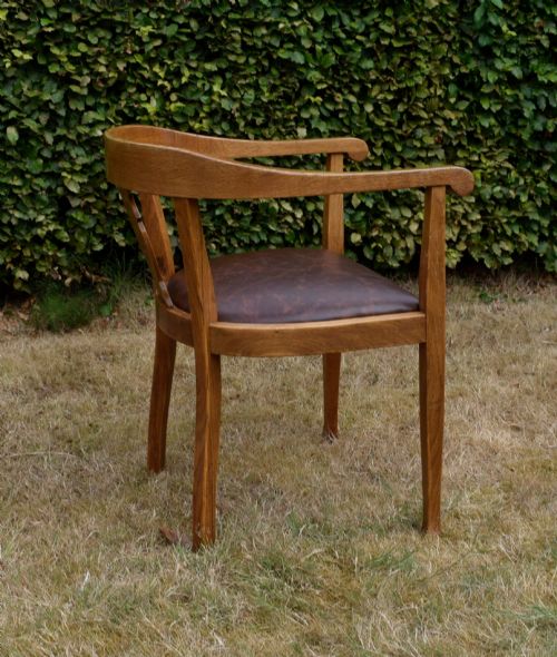 fig 6. An early 20th-century oak desk chair featuring a curved horseshoe backrest, a carved central splat, and a dark brown upholstered seat pad.