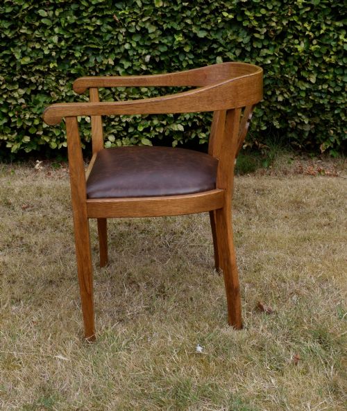 fig 7. An early 20th-century oak desk chair featuring a curved horseshoe backrest, a carved central splat, and a dark brown upholstered seat pad.