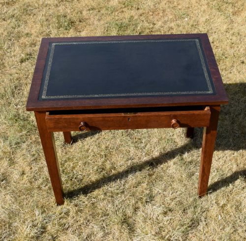 fig 4. A warm brown oak Arts and Crafts writing desk with a dark inset leather top, a single drawer with turned wooden knobs, and four square straight legs.