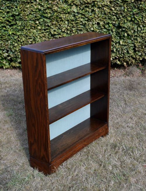 fig 1. A dark oak Art Deco open bookcase featuring three shelves and a light duck-egg blue textured back panel.