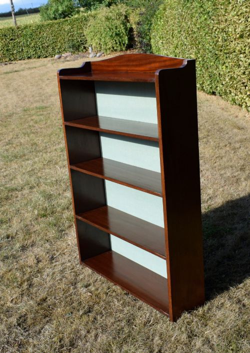 fig 1. A standing mahogany open bookcase featuring four horizontal shelves, a gently curved top upstand, and a light-coloured fabric back panel.