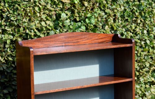 fig 5. A standing mahogany open bookcase featuring four horizontal shelves, a gently curved top upstand, and a light-coloured fabric back panel.