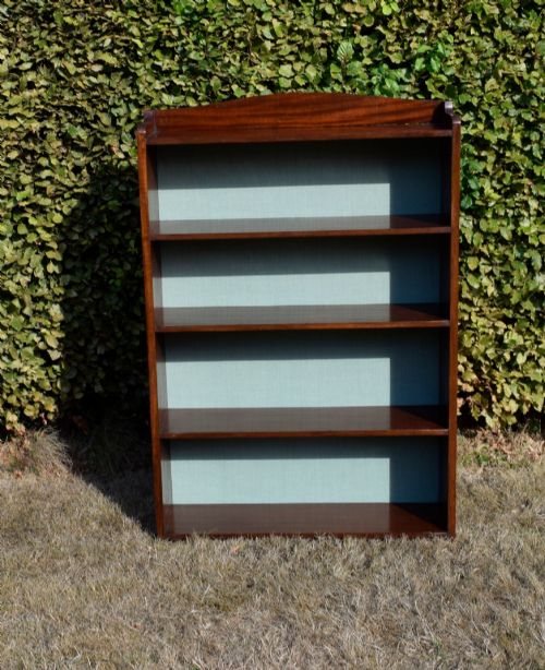 fig 6. A standing mahogany open bookcase featuring four horizontal shelves, a gently curved top upstand, and a light-coloured fabric back panel.
