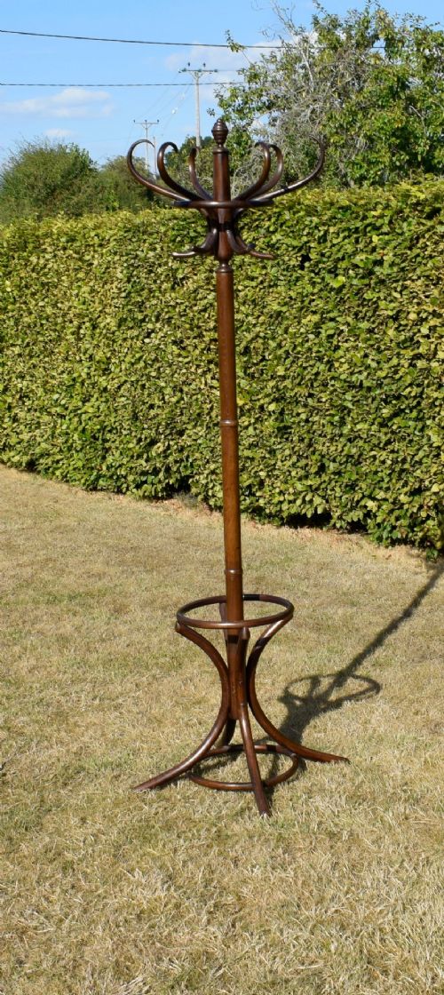 fig 1. A dark brown bentwood coat and hat stand featuring curved upper hooks, a turned central post, an umbrella ring, and curved tripod legs.