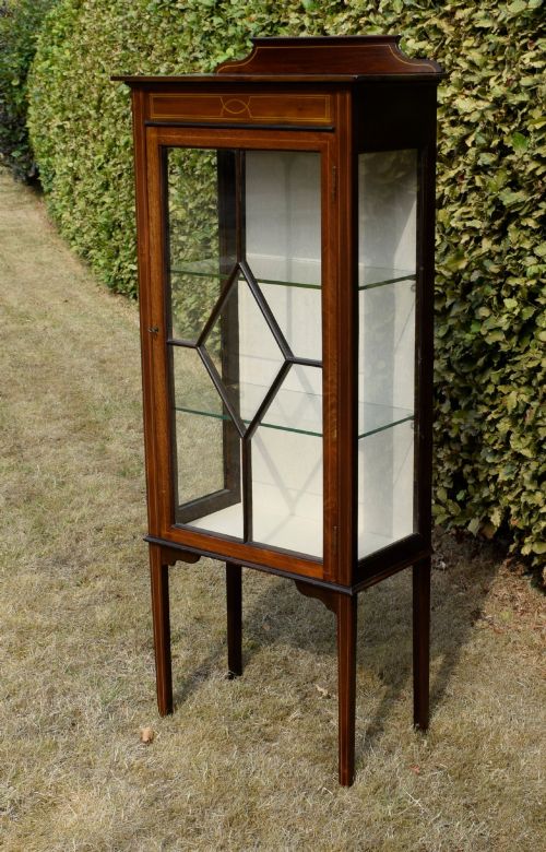 fig 2. An Edwardian mahogany display cabinet featuring satinwood inlay, a single door with a central diamond astragal glazing bar, glass shelves, and square tapered legs.