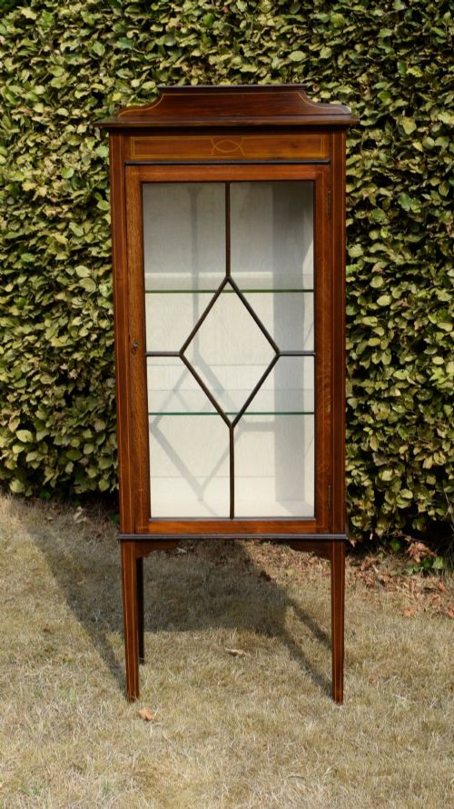 fig 6. An Edwardian mahogany display cabinet featuring satinwood inlay, a single door with a central diamond astragal glazing bar, glass shelves, and square tapered legs.