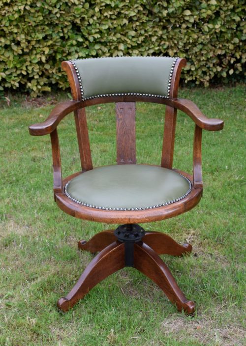fig 1. An early 20th-century oak swivel desk chair featuring a green leather padded seat and backrest trimmed with metal studs, supported by a four-spoke wooden base with a central iron mechanism.