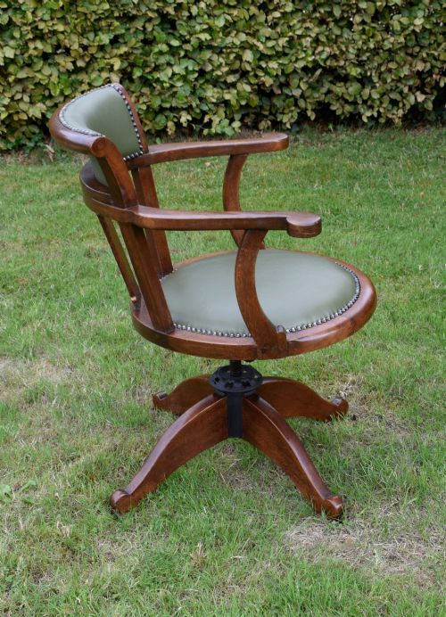 fig 5. An early 20th-century oak swivel desk chair featuring a green leather padded seat and backrest trimmed with metal studs, supported by a four-spoke wooden base with a central iron mechanism.