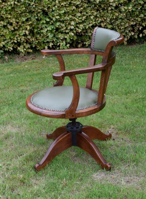 fig 6. An early 20th-century oak swivel desk chair featuring a green leather padded seat and backrest trimmed with metal studs, supported by a four-spoke wooden base with a central iron mechanism.
