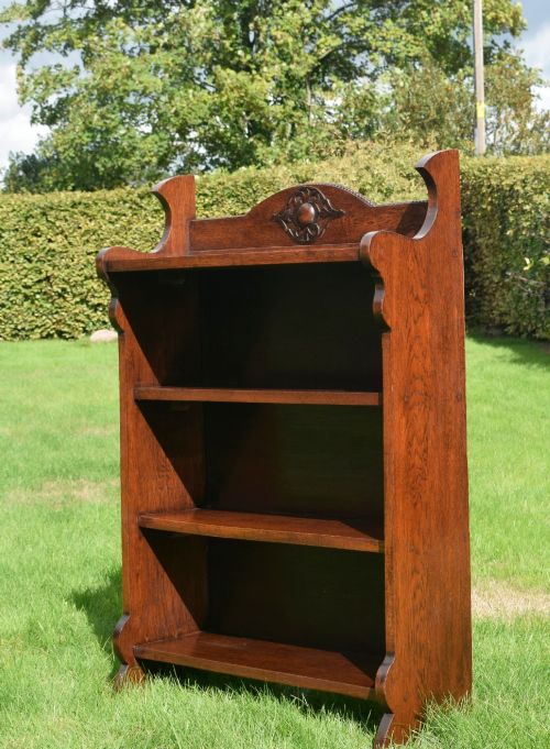 fig 3. An early twentieth-century open oak bookcase featuring a carved floral crest on the top gallery, shaped sides, and three fixed shelves.