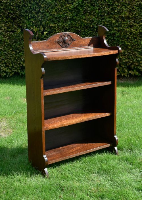 fig 4. An early twentieth-century open oak bookcase featuring a carved floral crest on the top gallery, shaped sides, and three fixed shelves.