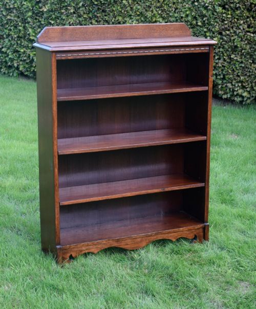 fig 1. An early 20th-century open dark oak bookcase with four shelves, a low top gallery, and a scalloped plinth base.