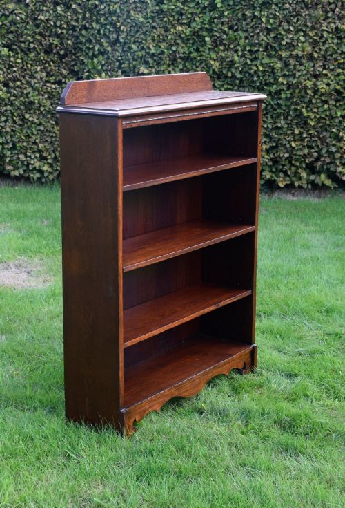 fig 3. An early 20th-century open dark oak bookcase with four shelves, a low top gallery, and a scalloped plinth base.
