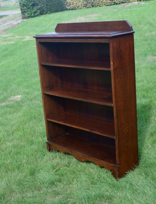 fig 6. An early 20th-century open dark oak bookcase with four shelves, a low top gallery, and a scalloped plinth base.