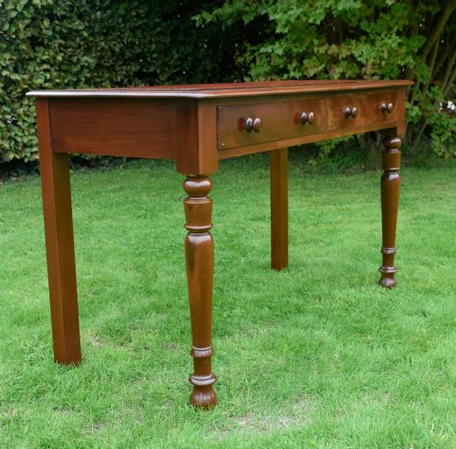 fig 2. A Victorian mahogany writing table with a red leather inset surface, two drawers with wooden knob handles, turned front legs, and square back legs.