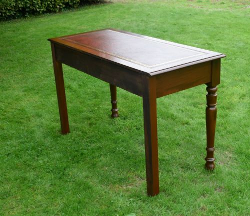 fig 3. A Victorian mahogany writing table with a red leather inset surface, two drawers with wooden knob handles, turned front legs, and square back legs.