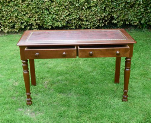 fig 6. A Victorian mahogany writing table with a red leather inset surface, two drawers with wooden knob handles, turned front legs, and square back legs.