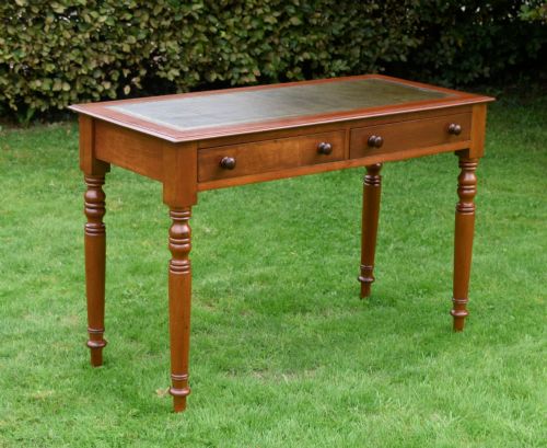 fig 1. A Victorian warm brown mahogany writing table featuring an inset green leather writing surface, two drawers with knob handles, and turned legs.