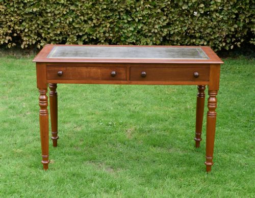 fig 2. A Victorian warm brown mahogany writing table featuring an inset green leather writing surface, two drawers with knob handles, and turned legs.