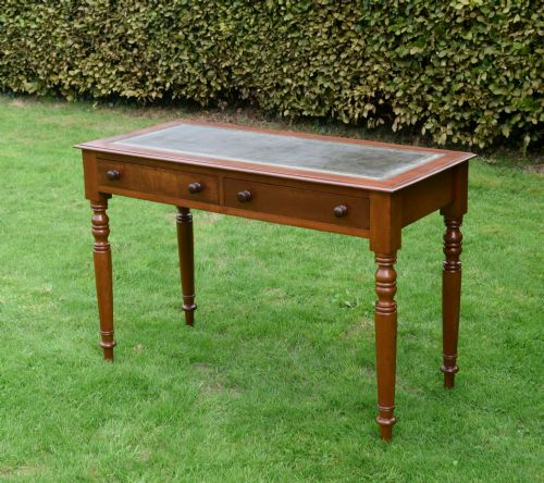 fig 3. A Victorian warm brown mahogany writing table featuring an inset green leather writing surface, two drawers with knob handles, and turned legs.