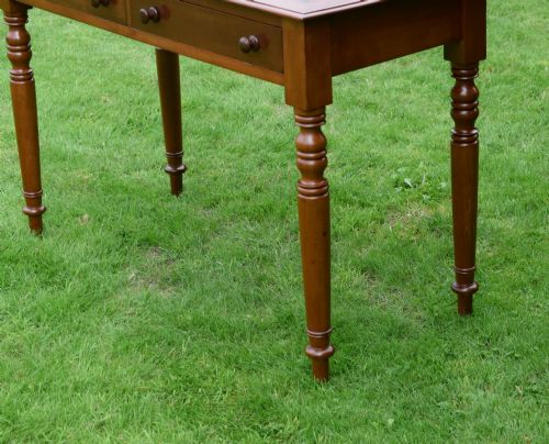 fig 5. A Victorian warm brown mahogany writing table featuring an inset green leather writing surface, two drawers with knob handles, and turned legs.